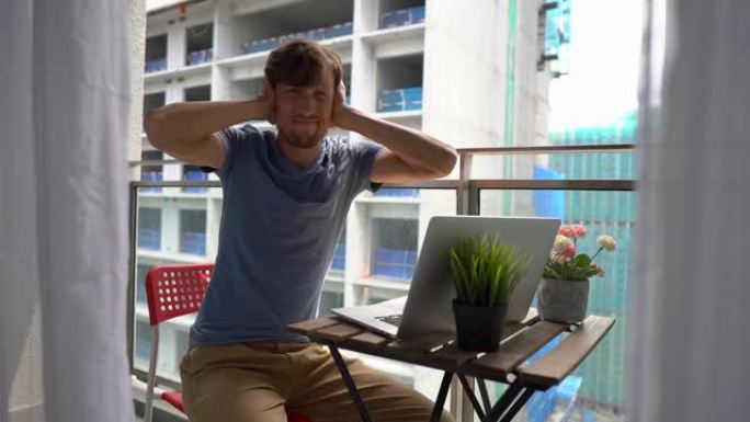 慢动作拍摄了一个年轻人坐在阳台上的笔记本，并遭受附近建筑工地产生的巨大噪音。大城市噪声污染的概念