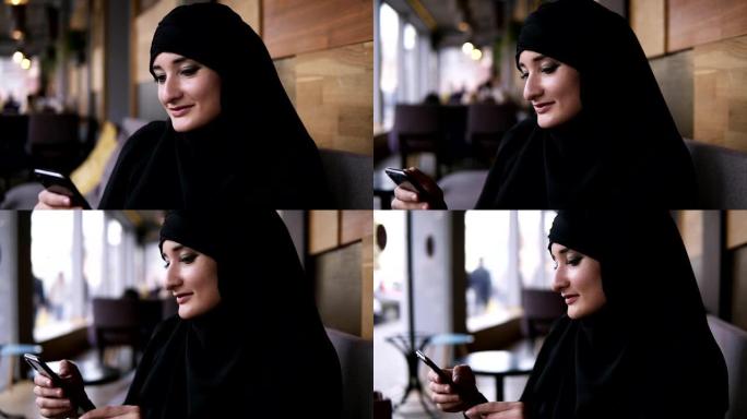 关闭穆斯林妇女在咖啡馆使用她的智能手机，与朋友在线聊天或浏览社交媒体，分享生活方式。享受、放松阅读信