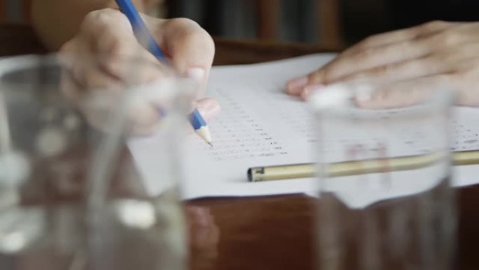 学校/大学的学生在化学教室里用手拿铅笔在光学表格上写试卷，在桌子上做期末考试。