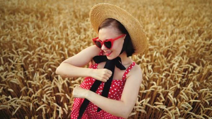 穿着红色连衣裙和草帽在金色麦田跳舞的迷人有趣的女孩。成功，复古风格，快乐，幸福概念