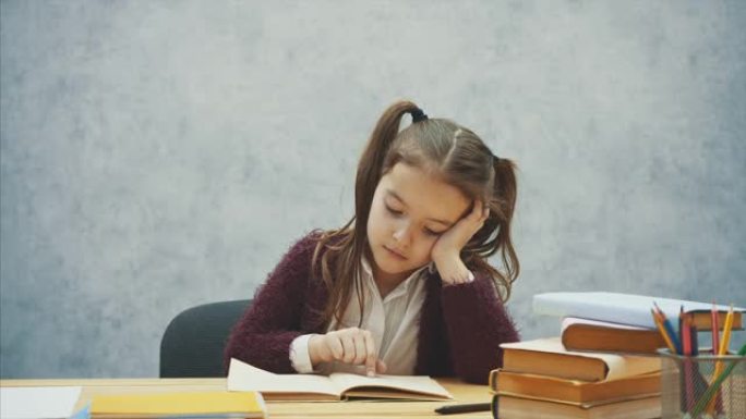 女婴看书坐在灰色的室内。女学生在学习课本。穿着校服的孩子很乐意看书。家庭训练一本有趣的儿童书。慢动作