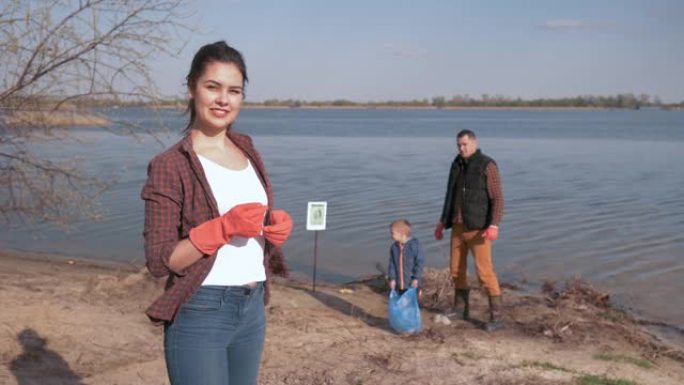 反对污染的年轻社会，微笑的女性志愿者的肖像在用塑料垃圾清理海滩时，对有小孩的家庭不专心的背景表示赞赏
