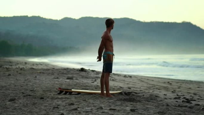 美丽的千禧一代年轻健康冲浪者在冲浪前日出时在海滩上做瑜伽