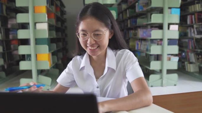 亚洲大学生女孩看书，用笔记本电脑和智能手机在公共图书馆做家庭作业