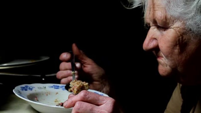 一位白发苍苍的老妇人在她破旧的旧房子里吃盘子里的袋子，生活在一个废弃的村庄里，有选择性的聚焦