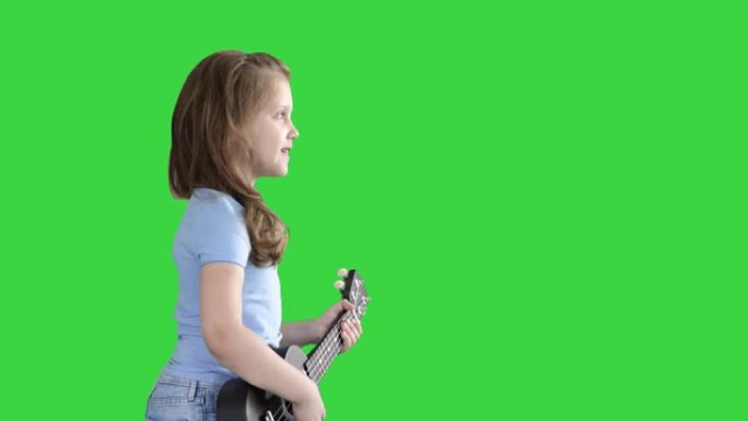 可爱的小女孩在绿屏上弹奏夏威夷四弦琴时走路和唱歌，色键