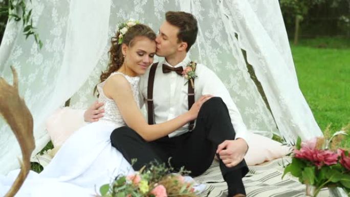 婚礼外面的新娘和新郎坐在白色装饰的帐篷里，一起亲吻。