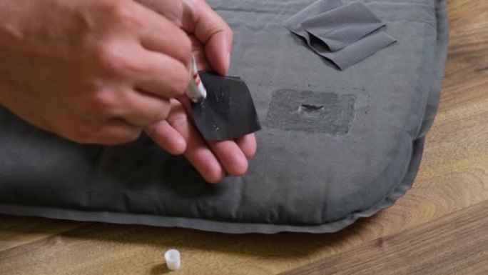 男性手在修理贴片上涂胶以固定帐篷睡垫中的穿刺处的特写。自修露营装备。