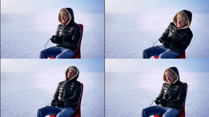 穿着暖和外套和兜帽的商人肖像，在冰冻的湖背景上用操纵杆玩电子游戏。
