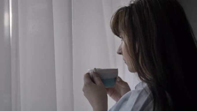 幸福的女人喝一口咖啡，享受味道，站在家里靠窗的地方