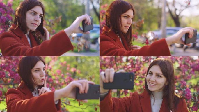 年轻迷人的红发女人在公园日落时在智能手机上的樱桃花或樱花花春天的背景上自拍