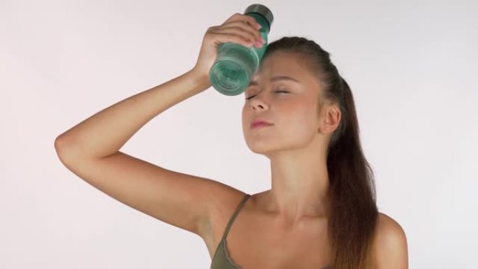 性感的女运动员拿着水瓶放在额头上，锻炼后休息