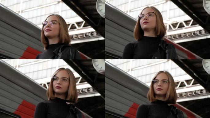 迷人的红发年轻女子短发，戴着眼镜，穿着黑色皮夹克，站在圣彼得堡美丽的历史悠久的维捷布斯克火车站，等待