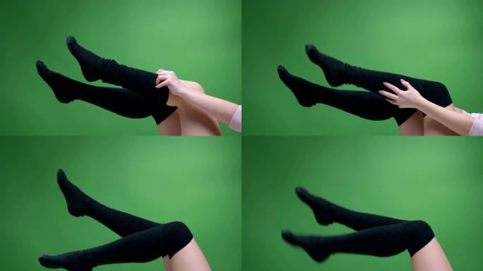 穿着可爱的黑色针织袜子的女性青少年腿特写镜头，背景孤立在绿色上，嬉戏地移动。女孩穿着她的膝盖袜子