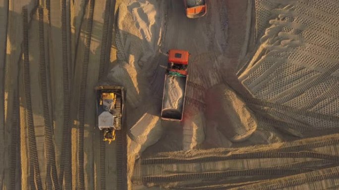 道路施工现场的施工现场。日落的夏日傍晚，用沙子的自卸车在建筑工地卸货。鸟瞰图