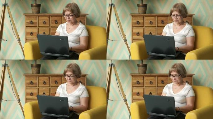 严肃的上了年纪的漂亮白种女人戴着眼镜坐在家里的椅子上用笔记本电脑工作。