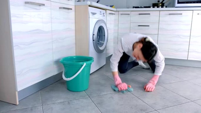 穿着粉红色橡胶手套的疲倦女人用布洗厨房地板。