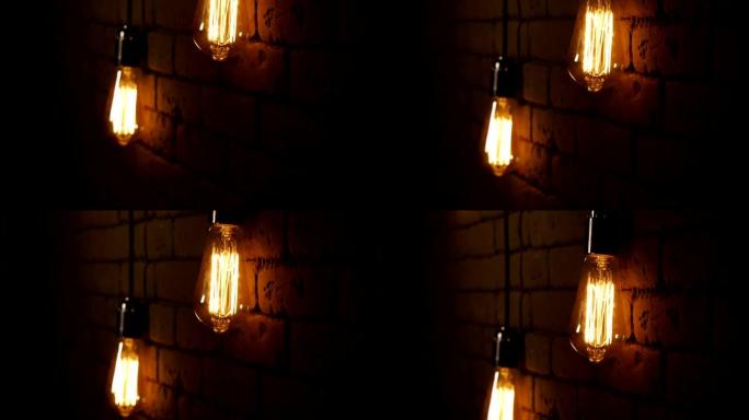 老式灯丝爱迪生灯泡。灯在黑暗中点亮。带有钨丝的白炽灯摆动。灯闪烁。向上慢动作。