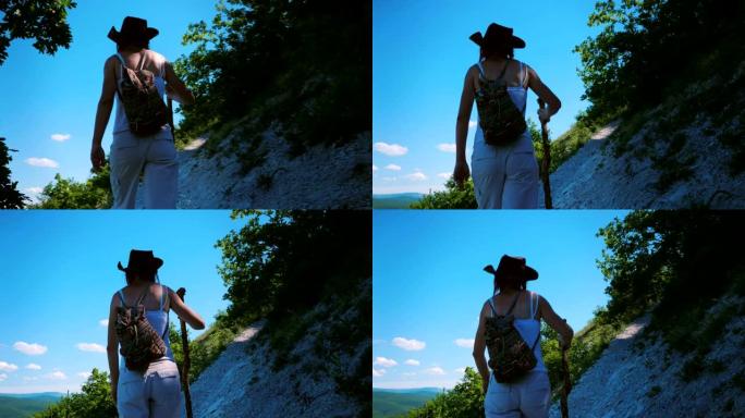 一个背着背包和木棍的女孩旅行者正沿着一条位于山中陡坡上的小路行走。