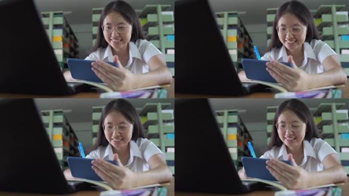 亚洲大学生女孩读书，工作和网上购物用笔记本电脑和智能手机在公共图书馆做家庭作业