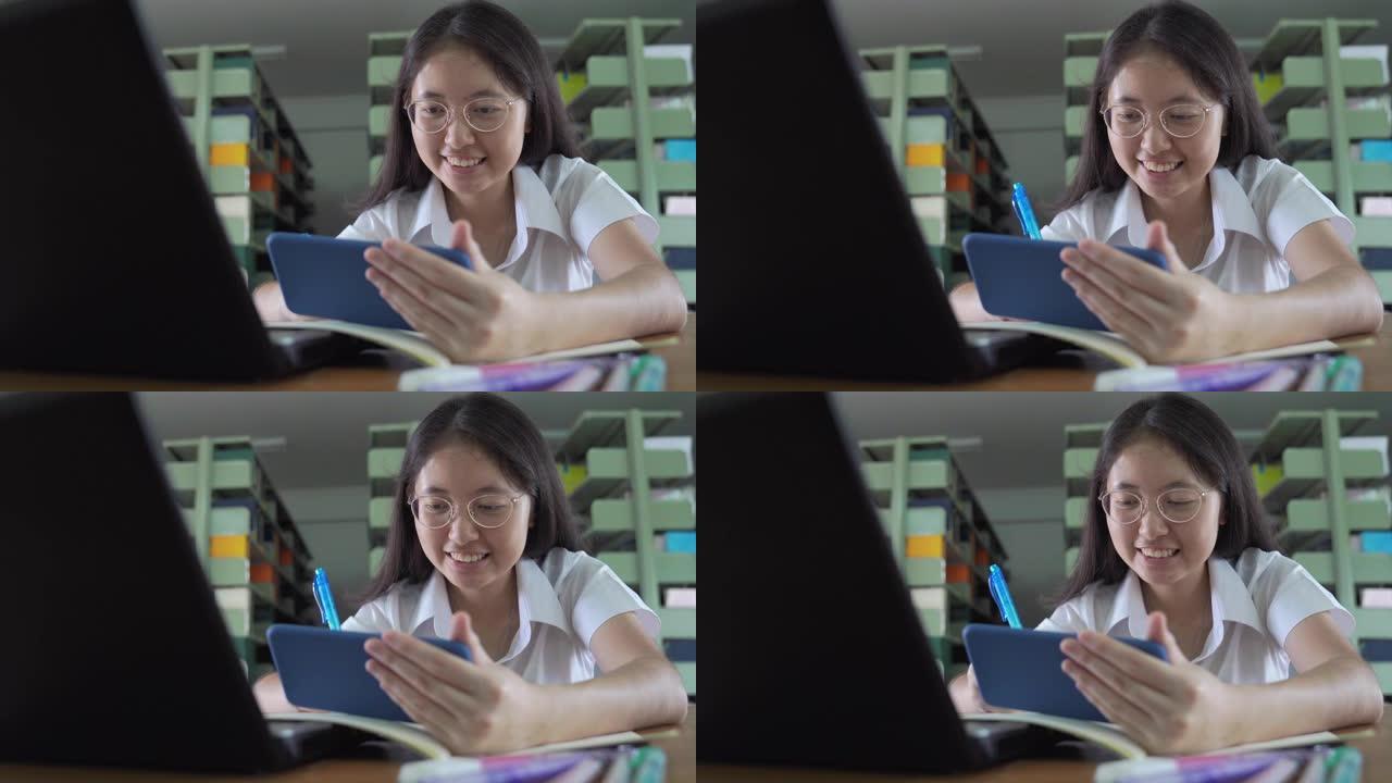 亚洲大学生女孩读书，工作和网上购物用笔记本电脑和智能手机在公共图书馆做家庭作业