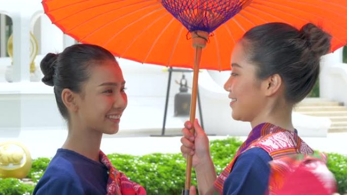 两名泰国年轻女子身穿泰国国家礼服套装，手持红色雨伞。欢迎来到泰国概念。