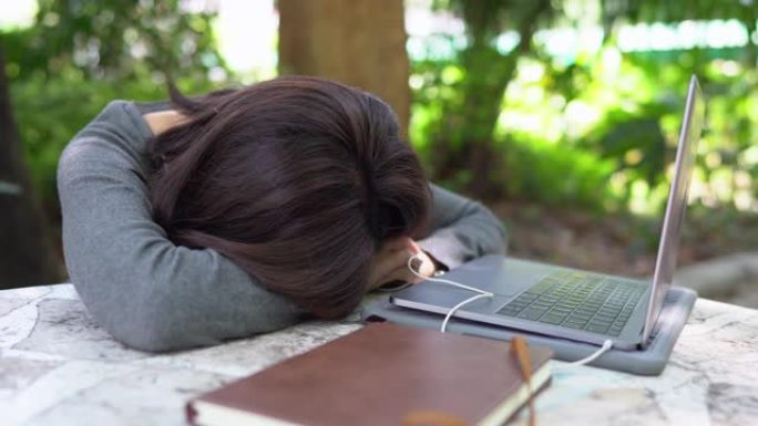 亚洲学生妇女在大学公园的笔记本电脑和笔记本电脑户外工作时小睡，潘开枪
