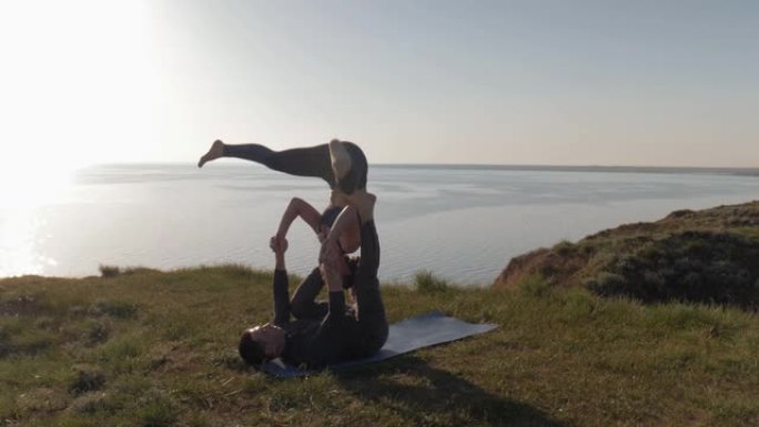 一起冥想，夫妻在日落和大海的背景下在山上做acro瑜伽改变姿势