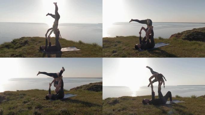 一起冥想，夫妻在日落和大海的背景下在山上做acro瑜伽改变姿势