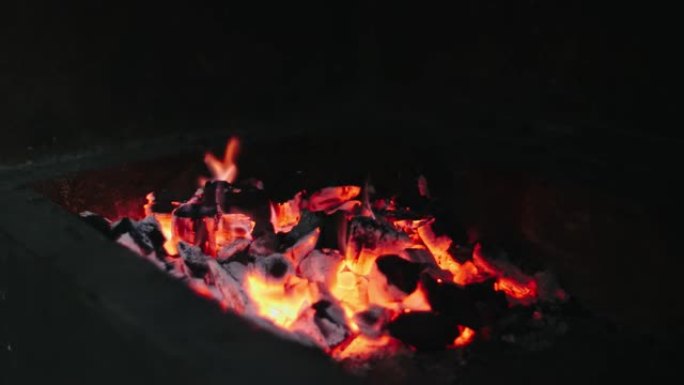 美丽的红色火从切片木材，深灰色黑色煤在金属火盆内。木头在火盆里燃烧着鲜黄色的火。火焰为烹饪烧烤做准备