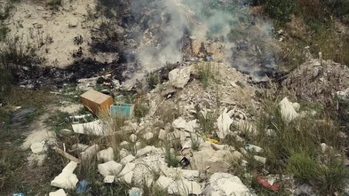 在非法垃圾场焚烧垃圾。鸟瞰图。塑料土壤污染。在城市郊区的植物中人们扔的闷烧垃圾上方冒烟。环境污染