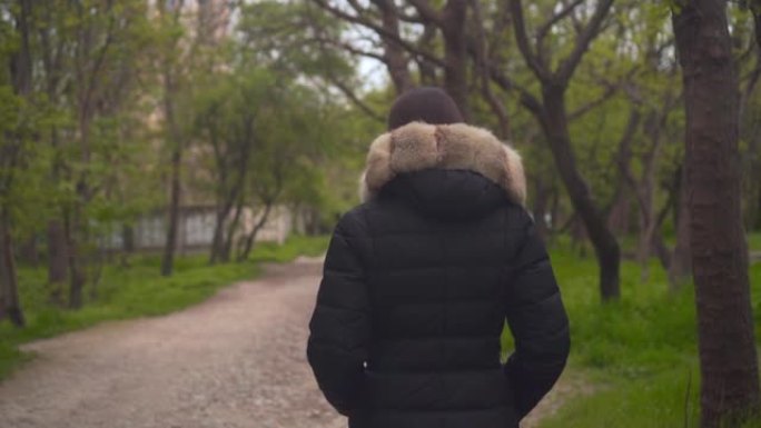 一个穿着温暖的黑色夹克的女孩穿过树林。女孩走在前面，摄像机跟着她。
