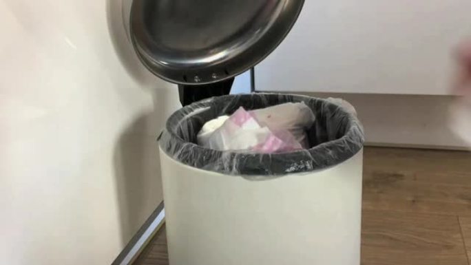 女人的手把用过的尿布一个接一个地放在家里的垃圾桶里。