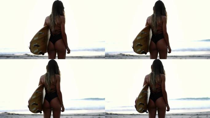 从海洋附近性感性感屁股年轻女孩的背后看。穿着时尚比基尼的冲浪者模特展示了它的运动屁股。