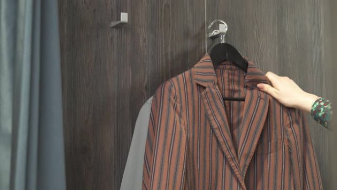 店员将男夹克带到试衣间的特写镜头。向客户提供衣服。多种选择。品牌服装