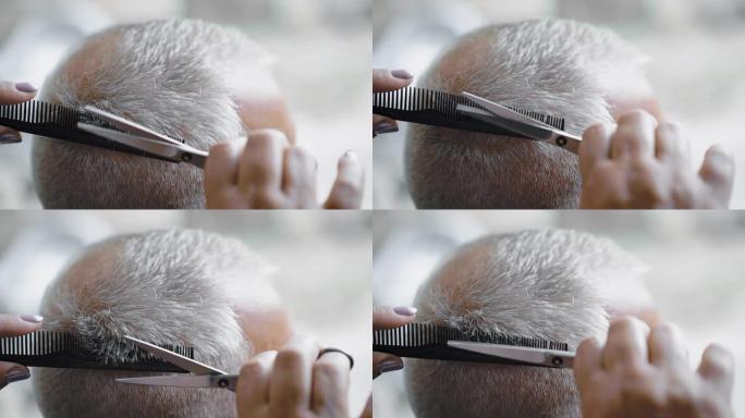 女美发师用剪刀剪白发男人。理发师用剪刀剪掉男人的头发。特写，慢动作。
