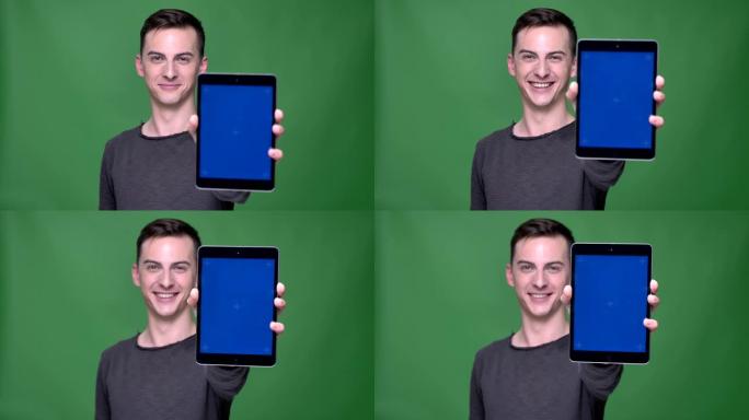 使用带有蓝色色度屏幕的平板电脑拍摄年轻英俊的高加索男性的特写镜头，背景隔离在绿色上