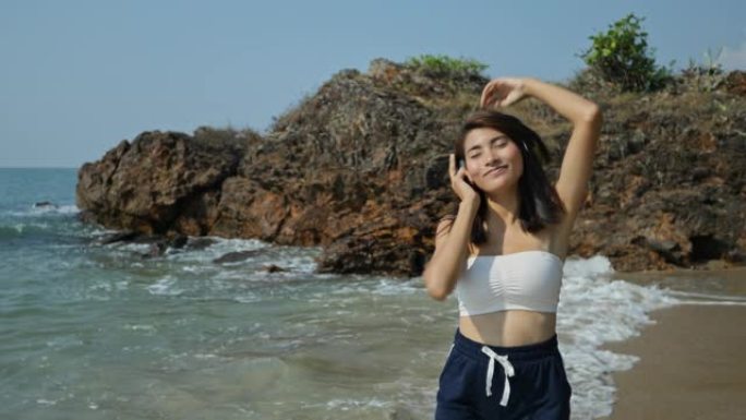 一个美丽的年轻女子在美丽的天空中快乐地在海滩上听着耳机里的音乐。