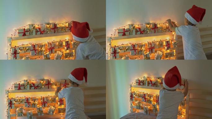 小男孩从挂在用圣诞灯照亮的床上的降临日历上拿了一份礼物。为圣诞节和新年概念做准备。降临日历概念