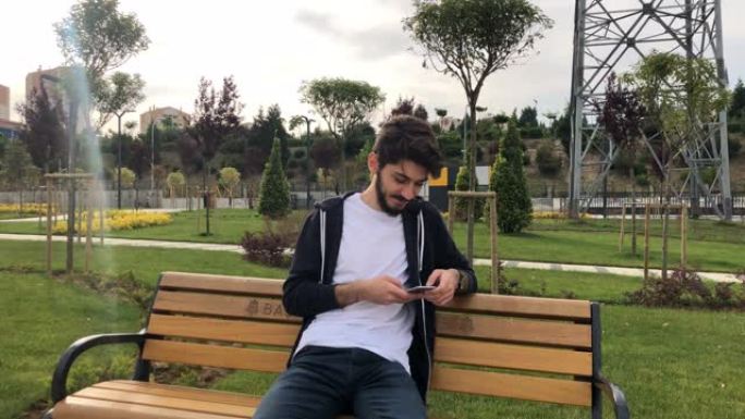 年轻快乐的男人坐在公园里使用智能手机