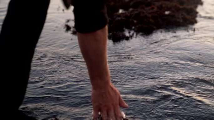 特写海水和穿着运动鞋的人的脚，迈出一步，用手触摸水，慢动作
