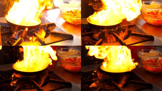 在餐厅的现代厨房里，无法识别的厨师在平底锅上烹饪flambe风格的菜肴。专业烹饪在燃气板上燃烧的煎锅
