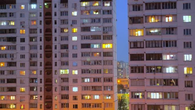 夜间照明建筑窗户的夜间时间流逝，人们住在带阳台的公寓里。用电概念。从下面看。晚上的城市街道