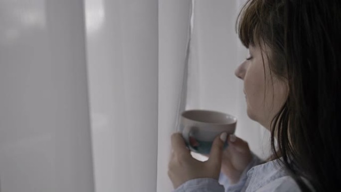 幸福的女人喝一口咖啡，享受味道，站在家里靠窗的地方