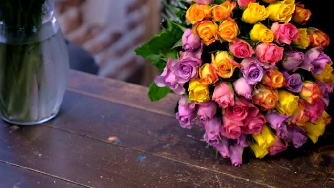 花店妇女作品用商店里五颜六色的玫瑰制成花束，双手特写。