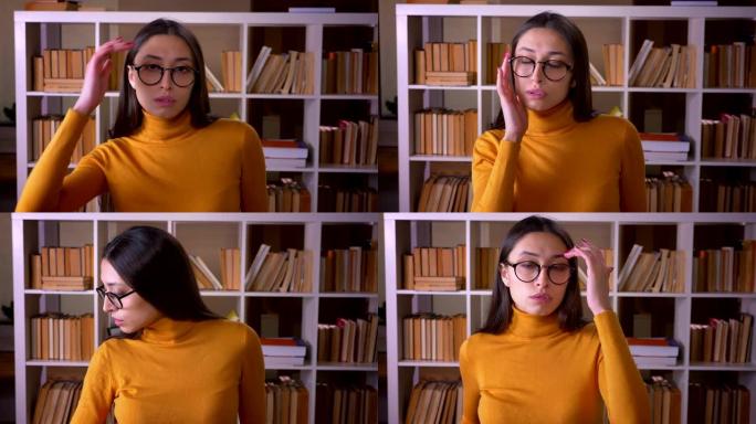 戴着眼镜的漂亮黑发女老师的肖像对着镜头摆姿势，在图书馆和它调情。