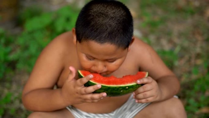快乐的亚洲胖男孩在户外吃西瓜