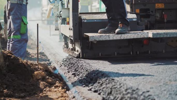 沥青摊铺机铺设热沥青到道路和工人控制。