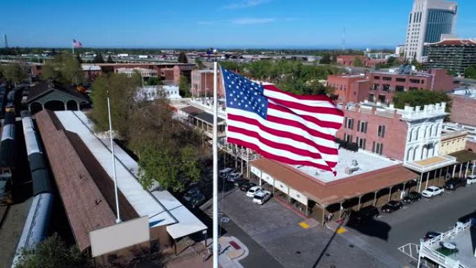 老萨克拉门托和遥远的萨克拉门托市中心前飘扬的美国国旗。无人机低空视频与轨道摄像机运动。