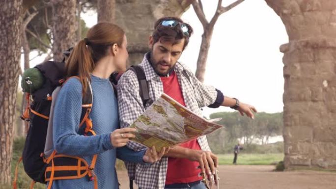 快乐的年轻夫妇背包客游客阅读地图指南，在罗马公园广场的罗马渡槽拱门附近迷失方向